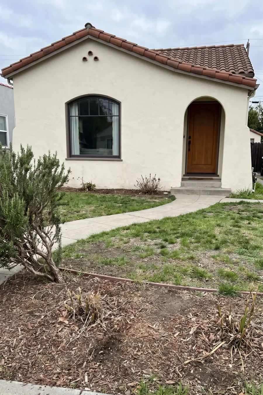 Before photo of a Spanish-style front yard with patchy lawn and bare beds